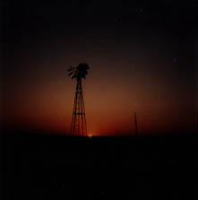 The dark silhouette of a broken windmill stands stark against the last light of the setting sun.